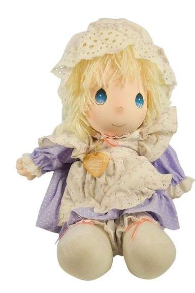 Precious Moments vintage cloth doll wearing a lavender and cream polka dot dress with lace trim and matching bonnet. The doll features signature blue eyes, soft blond yarn hair, and a heart-shaped “Precious Moments” pendant around her neck. In excellent pre-owned condition with charming, nostalgic appeal — a delightful collectible for fans of Precious Moments or vintage plush dolls. Measures approximately 12 inches tall. image