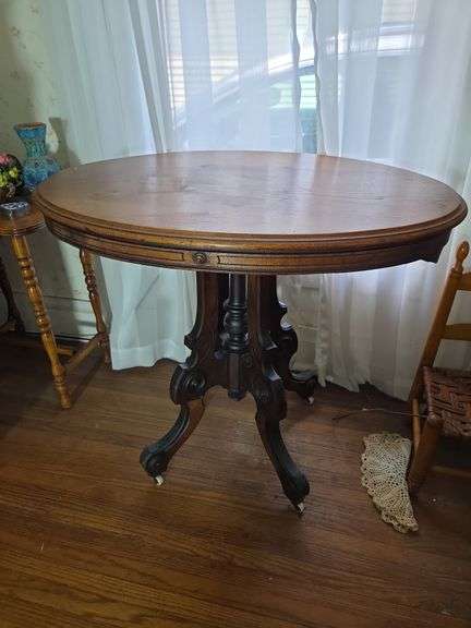 Round Wooden Table with Ornate Base and Rolling Feet image
