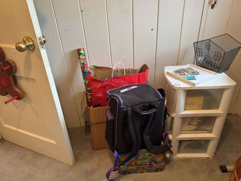 3 drawer plastic  cabinet with art supplies,backpack art supplies, box of  wrapping paper and behind door plastic hanging paper holder image