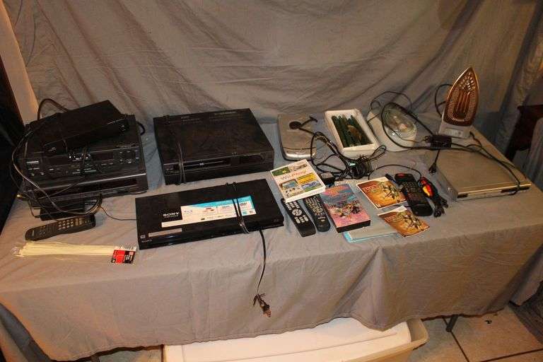 Daewoo VHS Player, Arris HDMI Box, Sony Blu Ray Player, VHS Player, TV Remotes, Candles, Kinyo VHS Tape Player, Protron DVD Player, Iron, and Misc.