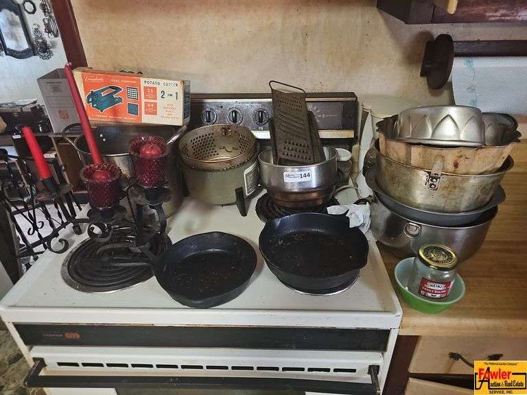 Selection of kitchen items including a Vaughan's potato cutter in the original box, two cast iron pans, metal bowls, a fry basket, grater and other kitchenware. image