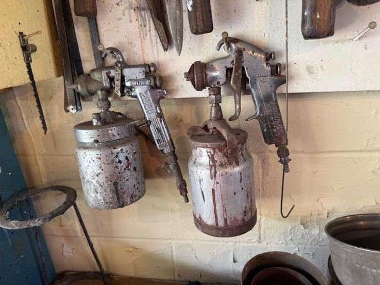 Tools hanging on wall, including wrenches, hammers, vice grips, saws, paint sprayers, bolt cutters, etc.