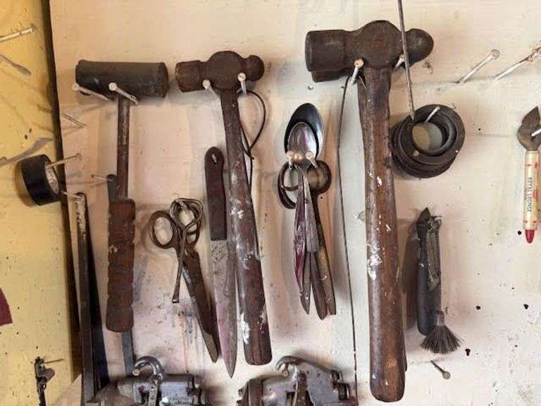 Tools hanging on wall, including wrenches, hammers, vice grips, saws, paint sprayers, bolt cutters, etc.