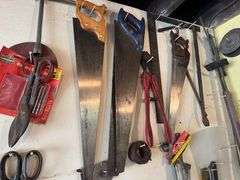 Tools hanging on wall, including wrenches, hammers, vice grips, saws, paint sprayers, bolt cutters, etc.