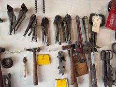 Tools hanging on wall, including wrenches, hammers, vice grips, saws, paint sprayers, bolt cutters, etc.