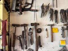 Tools hanging on wall, including wrenches, hammers, vice grips, saws, paint sprayers, bolt cutters, etc.