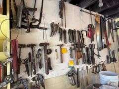 Tools hanging on wall, including wrenches, hammers, vice grips, saws, paint sprayers, bolt cutters, etc.
