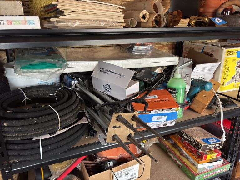 Large shelf full of hardware and tool type items, including soaker hose, hand tools, lights, tomato wall of waters, driveway markers