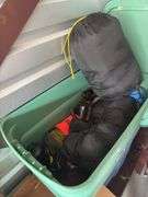 Large tote full of camping supplies, including sleeping bags, camping cookware set, propane burner, bag of rope and more