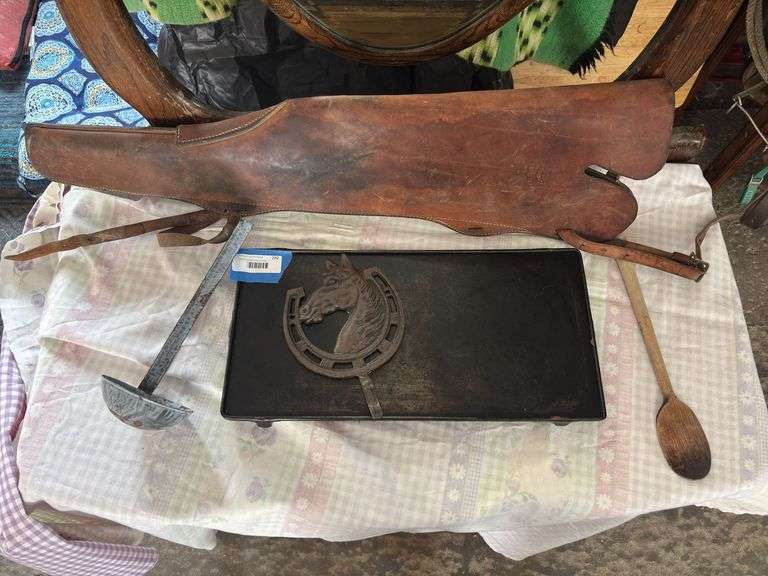 Antique cast-iron griddle, horseshoe wall hook, enamel spoon, wood spoon, and leather rifle scabbard, hunter brand image