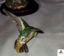 (2) MARURI HUMMINGBIRD FINE  PORCELAIN AND BRONZE STUDIO DESIGN H8905 ANNA'S HUMMINGBIRD WITH LILY, CIRCA 1989, BROKEN LIMB AND A RUBY THROATED HUMMINGBIRD WITH ORCHAD, LEAF MISSING OR BIRD, WING BROKEN - (2) HUMMINGBIRDS - (GREAT ROOM)