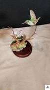 (2) MARURI HUMMINGBIRD FINE  PORCELAIN AND BRONZE STUDIO DESIGN H8905 ANNA'S HUMMINGBIRD WITH LILY, CIRCA 1989, BROKEN LIMB AND A RUBY THROATED HUMMINGBIRD WITH ORCHAD, LEAF MISSING OR BIRD, WING BROKEN - (2) HUMMINGBIRDS - (GREAT ROOM)