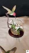 (2) MARURI HUMMINGBIRD FINE  PORCELAIN AND BRONZE STUDIO DESIGN H8905 ANNA'S HUMMINGBIRD WITH LILY, CIRCA 1989, BROKEN LIMB AND A RUBY THROATED HUMMINGBIRD WITH ORCHAD, LEAF MISSING OR BIRD, WING BROKEN - (2) HUMMINGBIRDS - (GREAT ROOM)