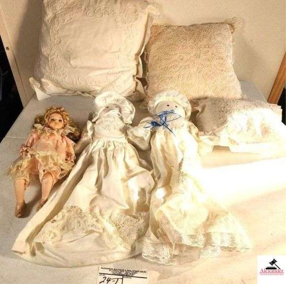 PORCELAIN HEAD DOLL - BLUE EYES - BLONDE HAIR CLOTH BODY - PORCELAIN HEAD, HAND, LEGS - (2) CLOTH DOLLS HAVE DECORATIVE DRESS WITH LACE TRIM AND HAT - (3) DECORATIVE PILLOWS - INCLUDES PLASTIC TOTE, NO LID - (GARAGE) image