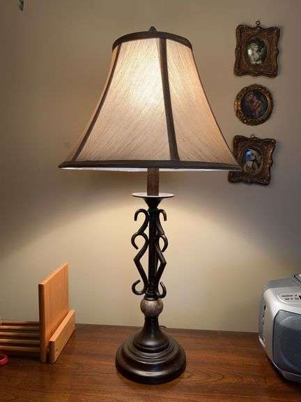 Traditional table lamp featuring a dark bronze-like finish, metal scroll base with marble-like cylindrical accent and a beige flare shade….25-1/2” tall image