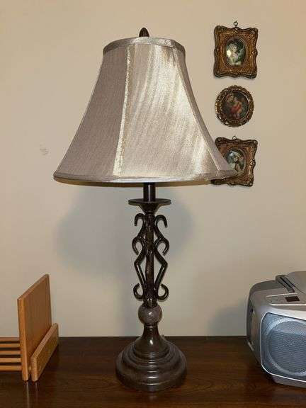 Traditional table lamp featuring a dark bronze-like finish, metal scroll base with marble-like cylindrical accent and a beige flare shade….25-1/2” tall image