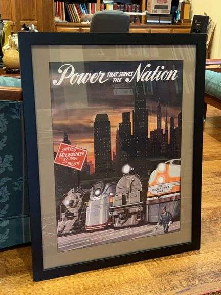 Framed vintage-style poster advertising the Chicago, Milwaukee, St. Paul and Pacific Railroad. The artwork features various trains set against a city skyline at sunset, with the prominent slogan "Power That Serves The Nation”…..32-1/4 x 40-1/2 image