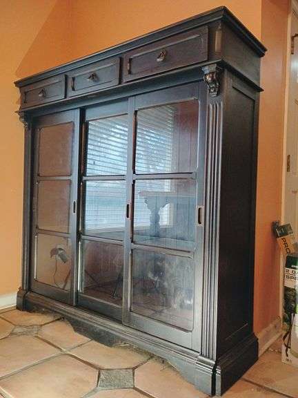 Ashley Furniture Rowley Creek Cabinet/ Hutch, Black rubbed finish, 3 drawers across top, glass front two doors on ends slide open, 64 1/4"T x 64"W x 19 1/2D, 2 glass shelves. BUYER IS RESPONSIBLE FOR REMOVAL. image