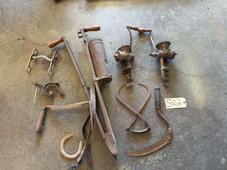 COLLECTION OF ANTIQUE FARM TOOLS AND KITCHEN IMPLEMENTS, INCLUDING A STEELYARD BALANCE SCALE, SUGAR NIPPERS, A CHERRY PITTER, A BILLHOOK OR SICKLE AND TWO HAND-CRANKED MEAT GRINDERS image