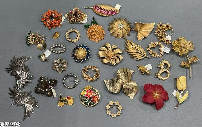 Vintage costume jewelry brooches, primarily in gold-tone metal with some silver-tone and enamel pieces, various designs such as floral motifs, leaves, a crown, a small tractor, and a B-shaped pin image