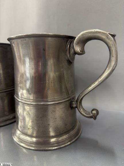 2 Pewter Tankards. Both Marked 'Quart' And Feature A Decorative Handle. One Mug Has GR 329 10 Stamped On It, And The Other Mug Has 1910 Stamped On It.
