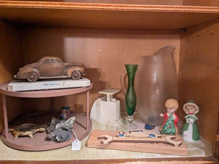 Bottom shelf: glass pitcher, carved 1940 Ford Coupe, metal wolf with spring loaded base, vase, holiday bells and misc. image